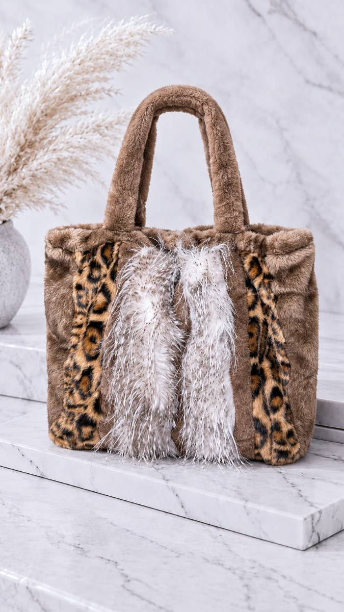 Shopper-Tasche aus Kunstfell mit Fransen-Detail auf Marmorstufen vor Trockenblumen-Dekoration in Leo