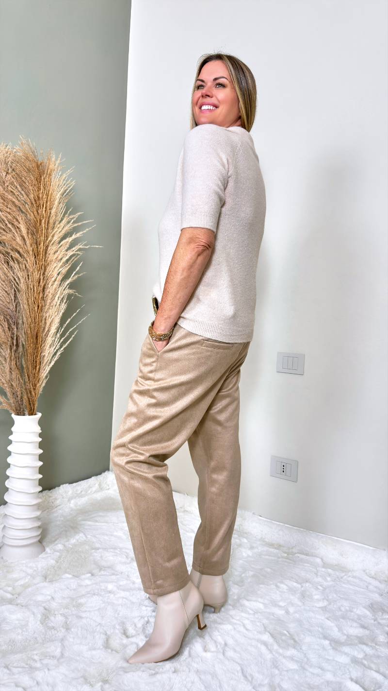 Frau trägt kurzärmeliges Strickshirt mit V-Ausschnitt und Kragen zu heller Stoffhose in Creme