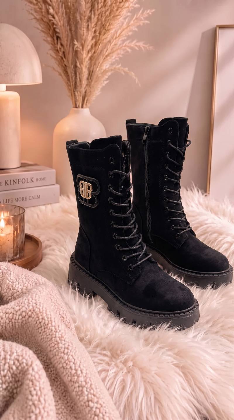 Schnürboots aus Velours mit Plateau-Sohle und goldenem Logo-Detail, seitlich auf Fell drapiert in Schwarz