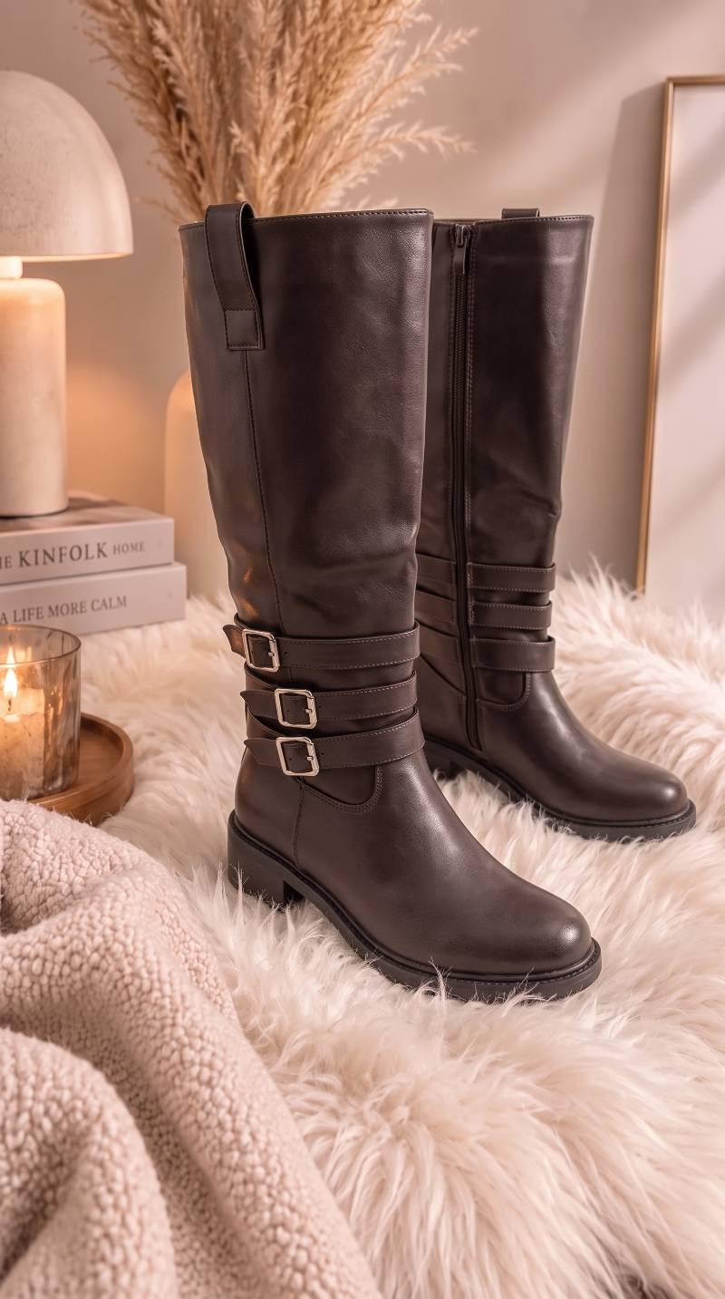 Zwei hohe Stiefel mit Schnallen-Riemen und Reißverschluss stehen auf einem flauschigen Fell in Schoko