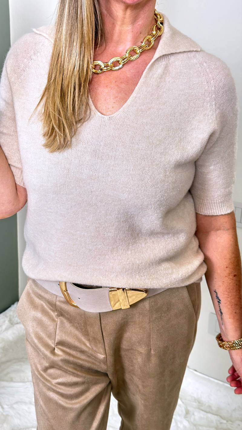 Frau trägt kurzärmeliges Strickshirt mit V-Ausschnitt und Kragen zu heller Stoffhose in Creme